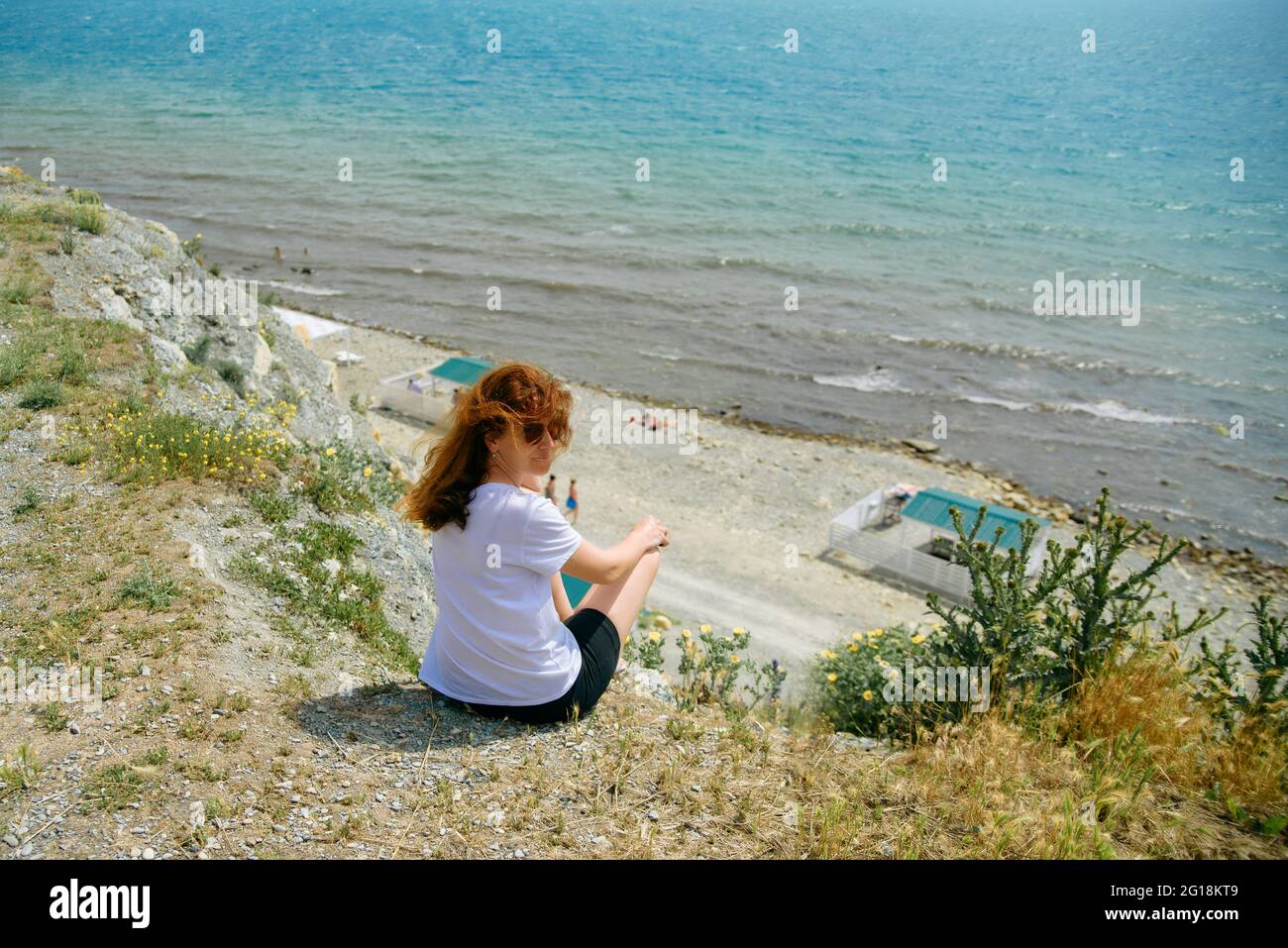 Felice ragazza godendo della vista mare dall'alto, la ragazza in una T-shirt bianca si siede su una scogliera e ammira il mare Foto Stock