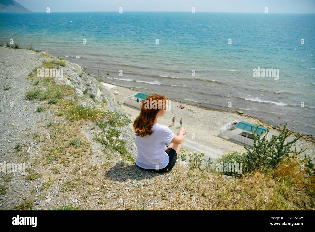 Felice ragazza godendo della vista mare dall'alto, la ragazza in una T-shirt bianca si siede su una scogliera e ammira il mare Foto Stock