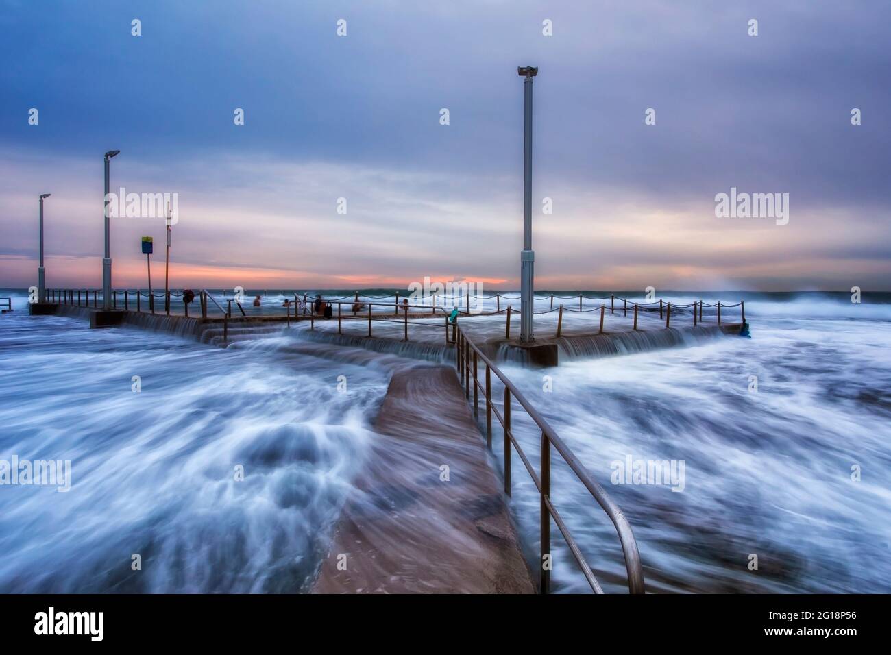 Alta marea alla spiaggia di Mona vale - onde che scorrono sulla piscina rocciosa all'alba. Foto Stock