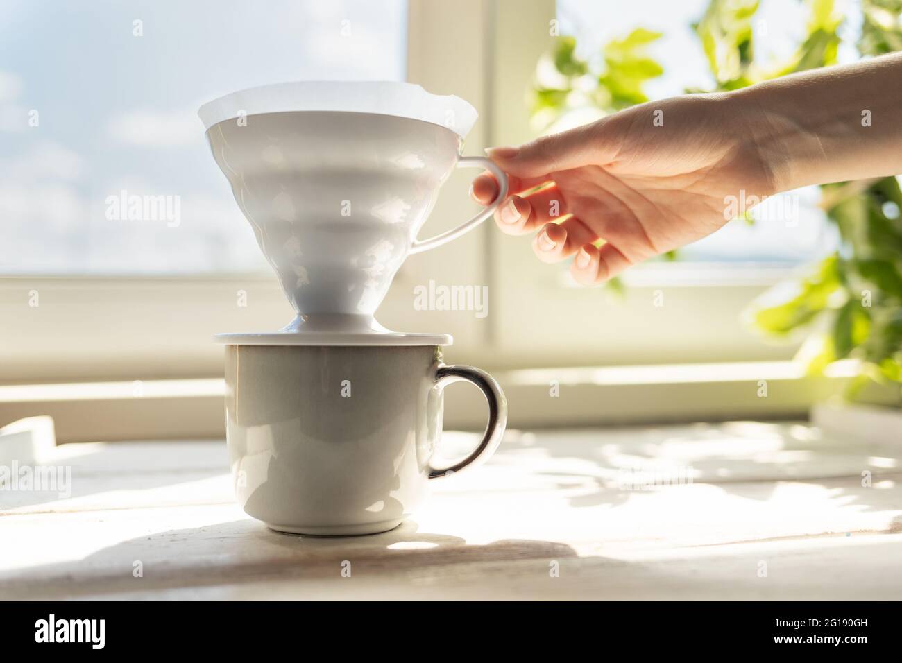Una mano femminile rimuove un imbuto con un filtro dalla tazza. Modalità alternativa di erogazione del caffè. Filtro V60 con caffè macinato estratto. Vista laterale. Foto Stock