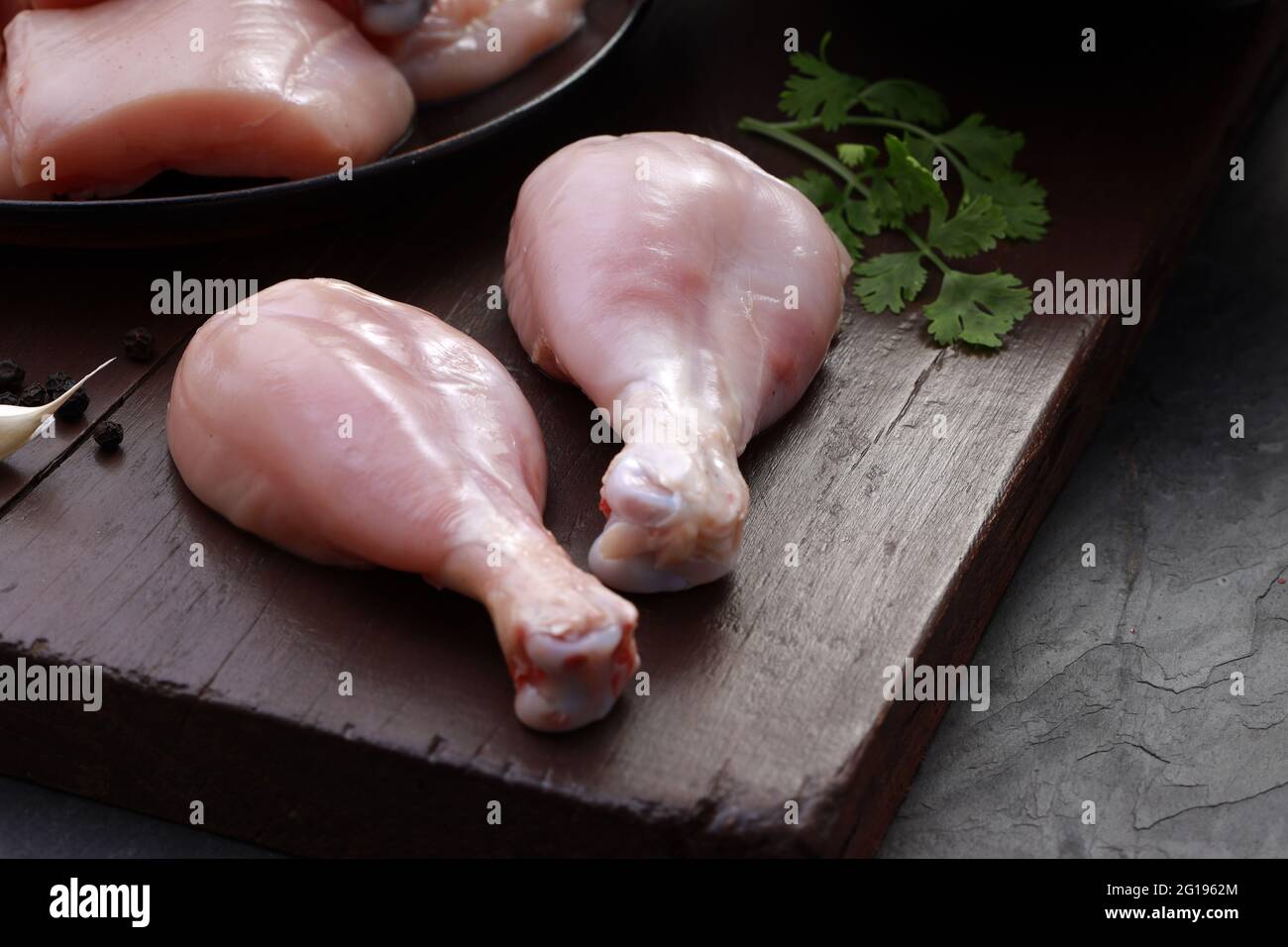 I tagli grezzi di pollo combo, combinazione di tagli di curry di pollo senza pelle, tagli di frittura di pollo e due bastoncini disposti su una tavola di legno con foglia di coriandolo Foto Stock