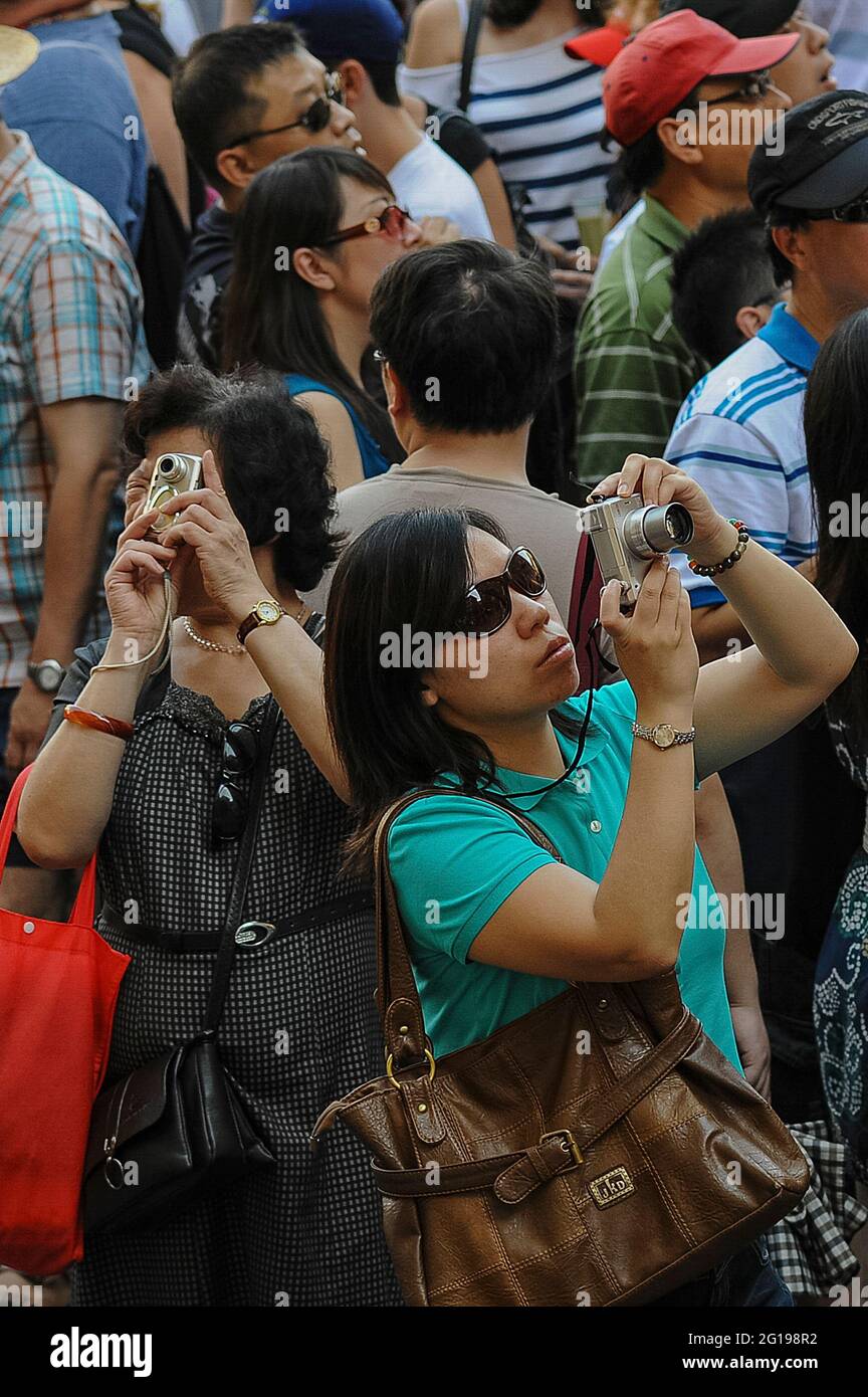 Due donne asiatiche catturano immagini digitali dei luoghi d'interesse nell'affollata Piazza della Signoria, il cuore storico di Firenze, capitale regionale della Toscana, Italia, a metà luglio, vicino al culmine dell'alta stagione estiva. Tra le attrazioni della ‘Dtroviamo il Palazzo Vecchio, la statua del Cavido di Michelangelo, la Fontana di Nettuno o la Fontana del Nettuno e la Loggia dei Lanzi, risalente al XIV secolo, unica galleria di sculture in rilievo da cui è stata scattata questa fotografia. Foto Stock