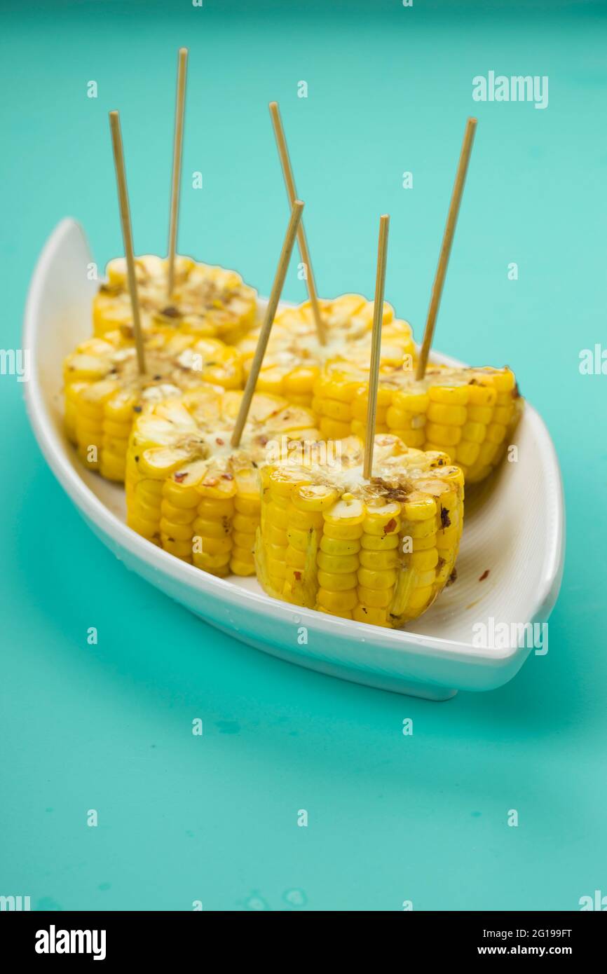 Mais, uno spuntino fatto con mais maturo e guarnito con fiocchi di peperoncino e miele sistemato in una bella tavola bianca che viene posta su un ghiaccio solido Foto Stock