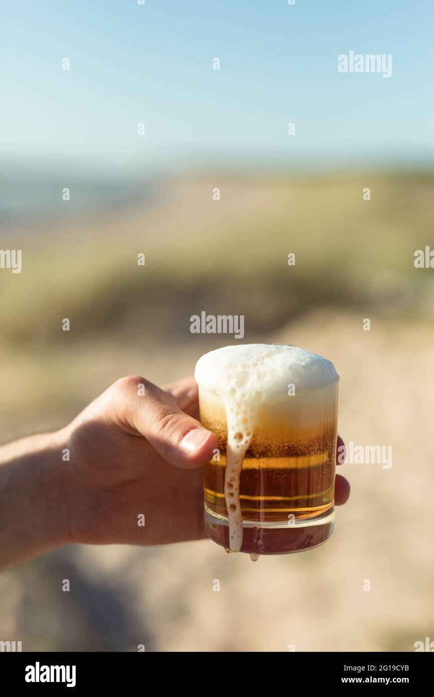 Celebrando la vita, uomo che tiene un bicchiere di birra lager in spiaggia Foto Stock