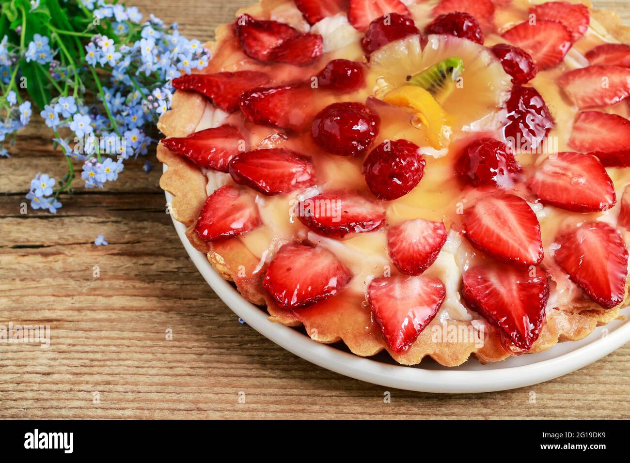 Crostata di fragole su tavola di legno marrone e bouquet di non dimenticare di me fiori. Foto Stock