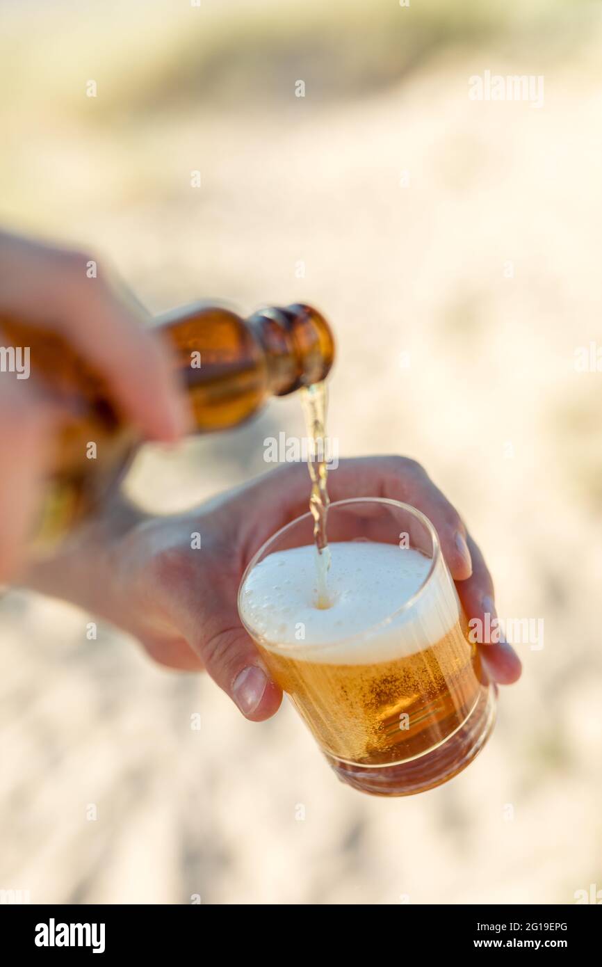 Uomo che versa la birra lager in un bicchiere sulla spiaggia Foto Stock