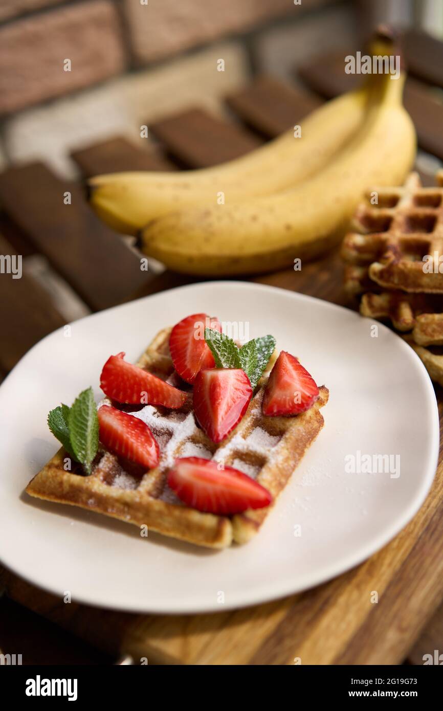 Vista della colazione, waffle belgi con fragola e banana con menta su sfondo di legno Foto Stock