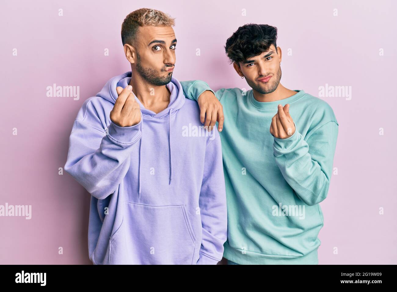 Coppia omosessuale gay in piedi insieme indossando abiti casual facendo gesto di denaro con le mani, chiedendo il pagamento dello stipendio, business milionario Foto Stock