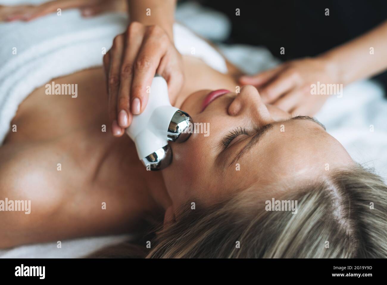 La giovane donna bionda ama il massaggio viso con un massaggiatore viso microcorrente nel centro benessere, concediti un po' di relax. Cura professionale del corpo Foto Stock