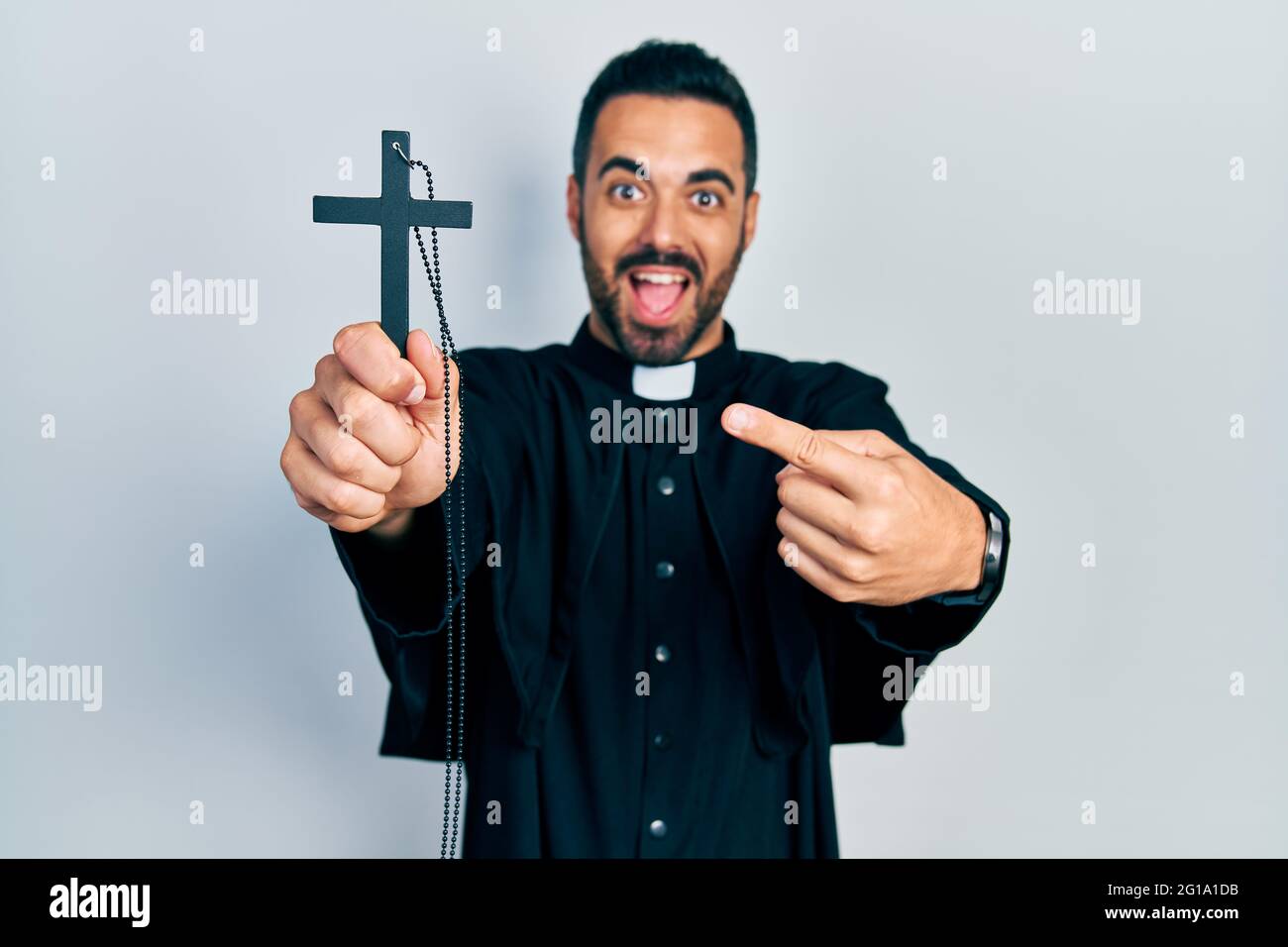 Bell'uomo prete ispanico con barba che tiene la croce cattolica sorridendo  felice indicando con mano e dito Foto stock - Alamy