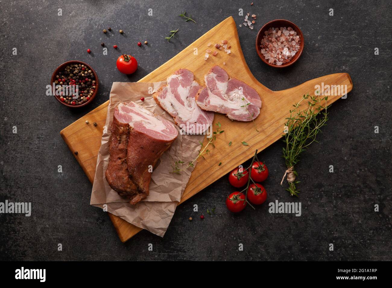 Gammon affumicato a fette su tavola di legno con aggiunta di erbe fresche e spezie aromatiche. Prodotto naturale da azienda agricola biologica, prodotto da me tradizionale Foto Stock