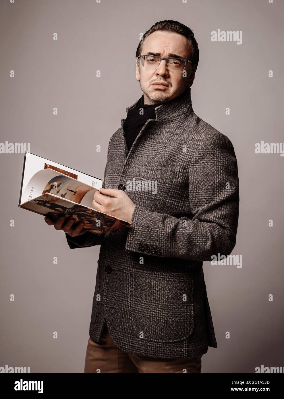 Ritratto di uomo intellettuale snobby critico letterario in giacca a scacchi e sciarpa nera guardando attraverso il nuovo libro Foto Stock