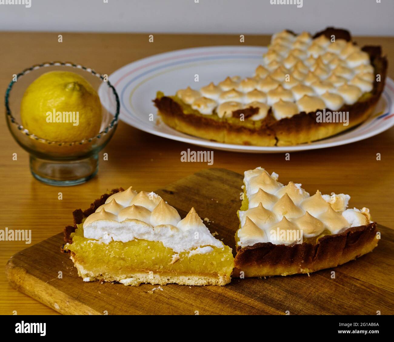 Due fette di torta di limone sul tavolo da taglio decorate con un limone e il resto della torta Foto Stock