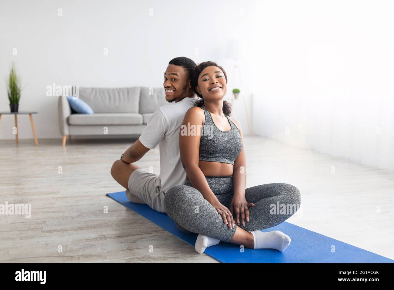 Una coppia afro-americana sorridente che si rilassa dopo una pratica di yoga, seduta sul tappetino fitness di nuovo in dietro, sorridendo alla macchina fotografica Foto Stock