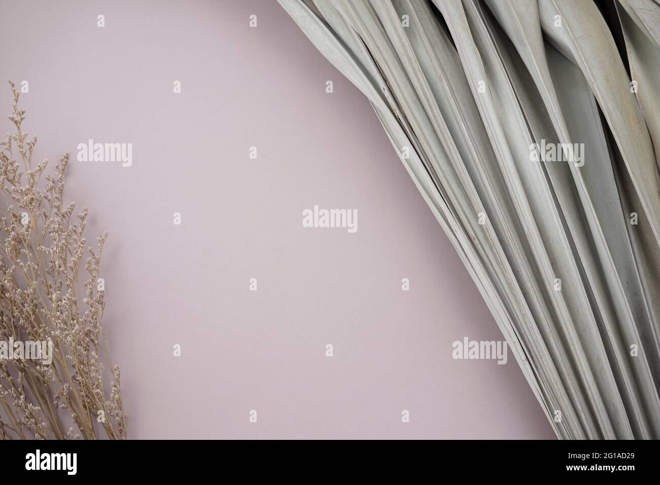 Foglie di palma secche e bouquet di fiori cespugliosi e appassiti adagiati su sfondo grigio-viola neutro color argento. Foto Stock