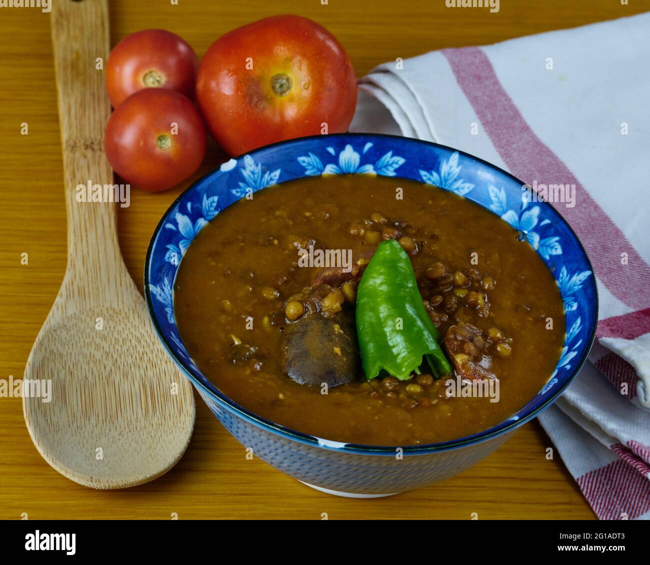 Zuppa di lenticchie fatta in casa con salsicce di maiale chiamato chorizo, salsiccia di sangue chiamato Morcilla e pepe verde in una ciotola decorata con pomodori, un cucchiaio e. Foto Stock