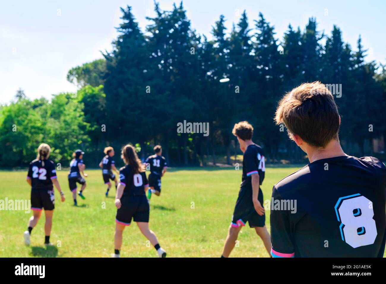 Gruppo di giovani adolescenti in squadra indossare giocare una partita di frisbee nel parco oudoors. L'uomo lancia un frisbee ad un compagno di squadra in una partita di frisbee finale. Foto Stock
