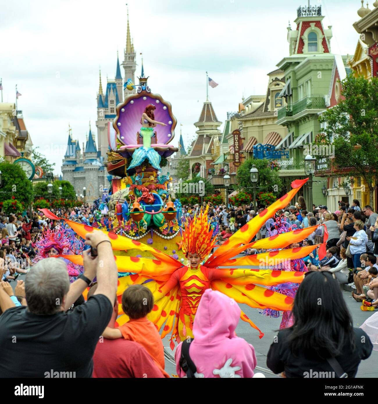 Suonatore vestito arancione e giallo, con il galleggiante Little Mermaid, in Festival of Fantasy Parade, Magic Kingdom Park, Walt Disney World, Orlando, Florida Foto Stock