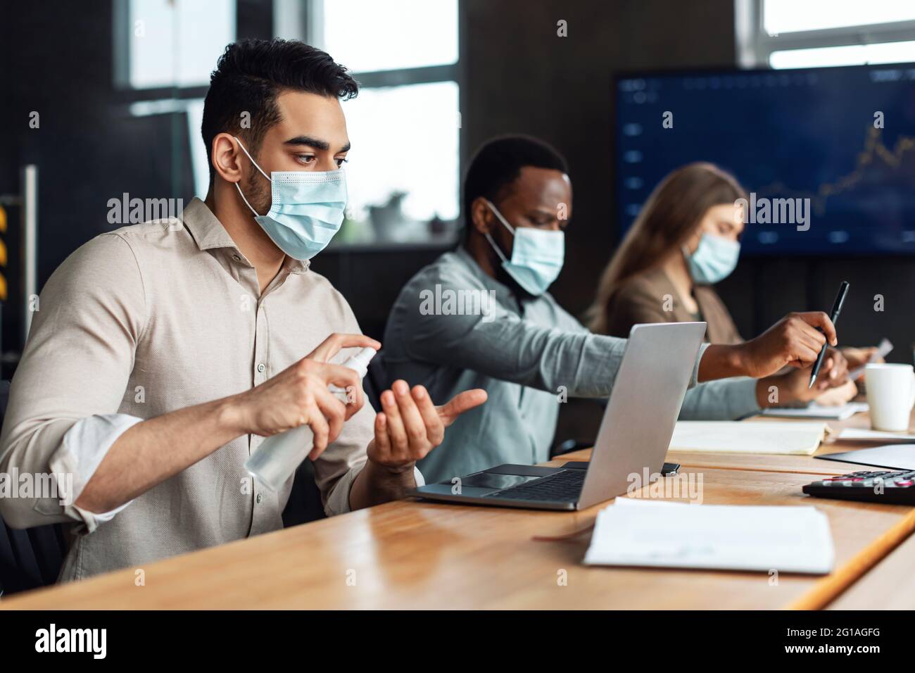 Colleghi internazionali che indossano maschere mediche utilizzando igienizzatore sulle mani Foto Stock