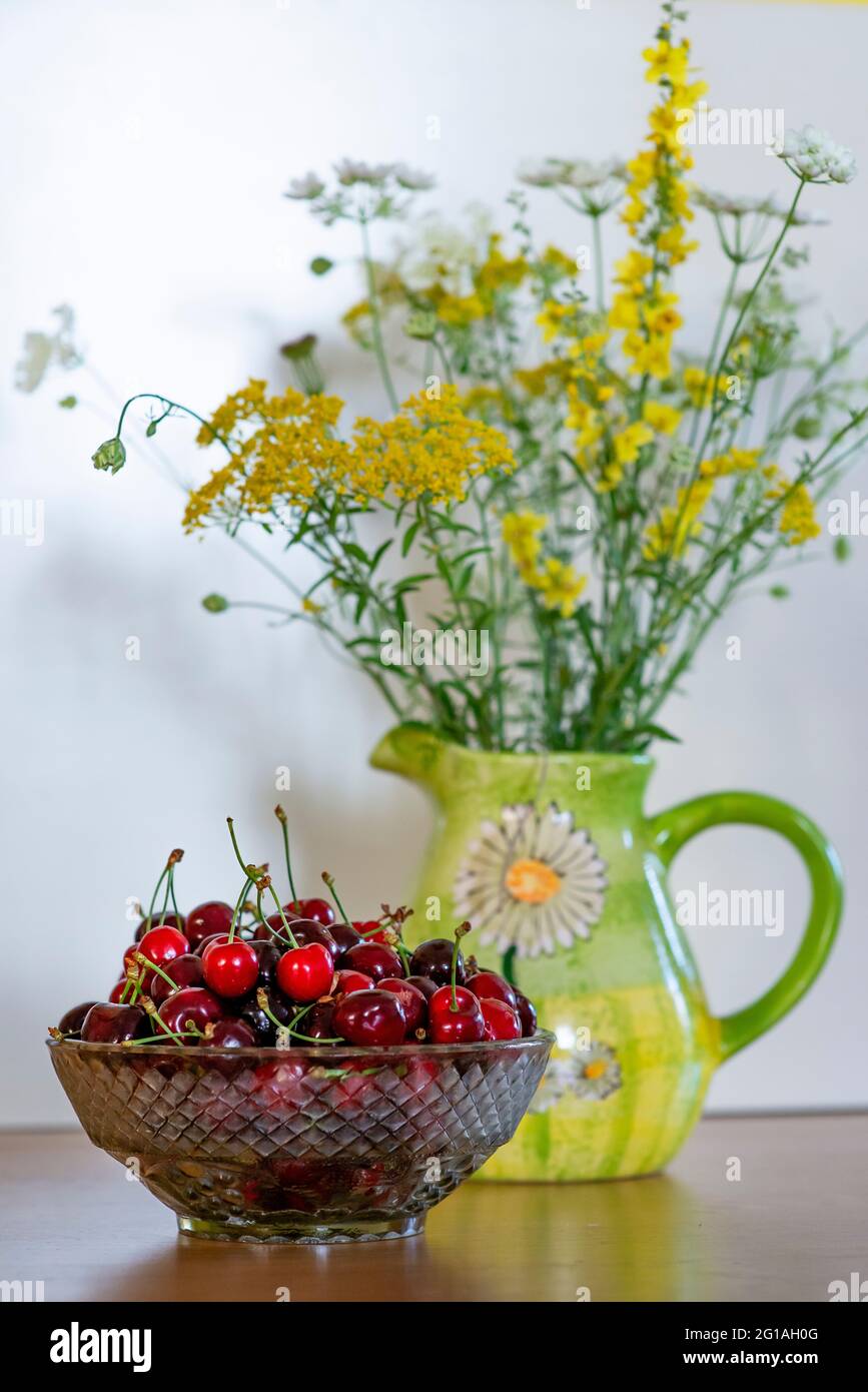 Estate still life - ciotola di ciliegie e un mazzo di fiori selvatici in un vaso Foto Stock