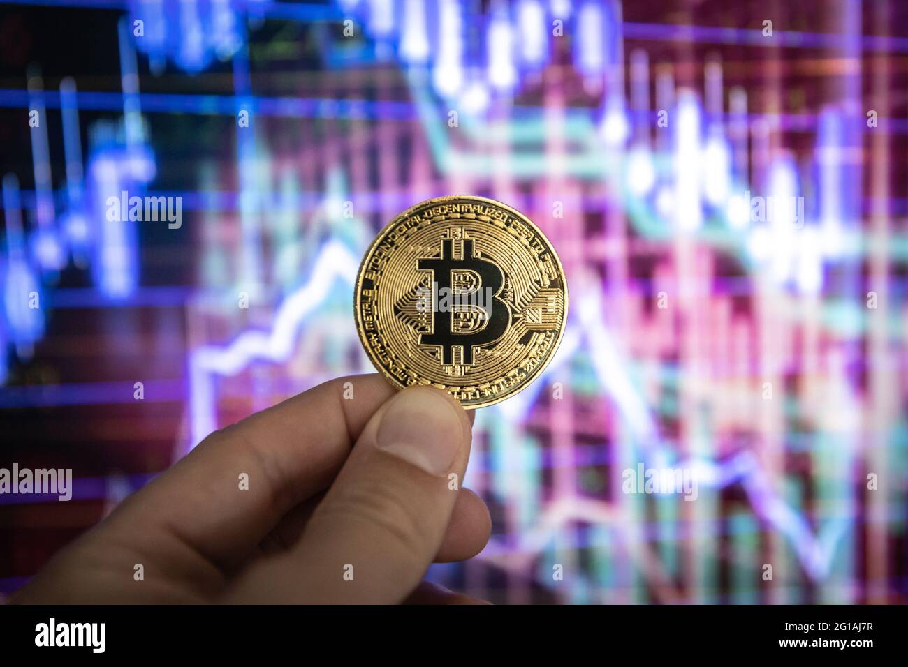 Moneta fisica Bitcoin davanti a grafici e grafici colorati. Foto Stock