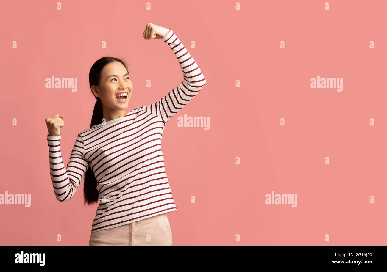 Grande gioia per la giovane donna asiatica che celebra il successo con Raised Fists Foto Stock