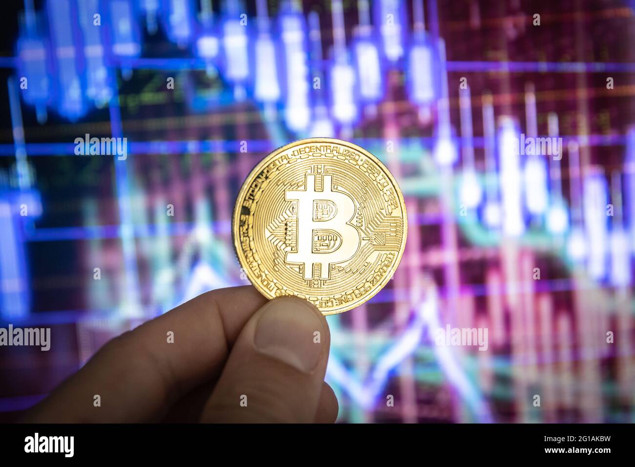 Moneta fisica Bitcoin davanti a grafici e grafici colorati. Foto Stock