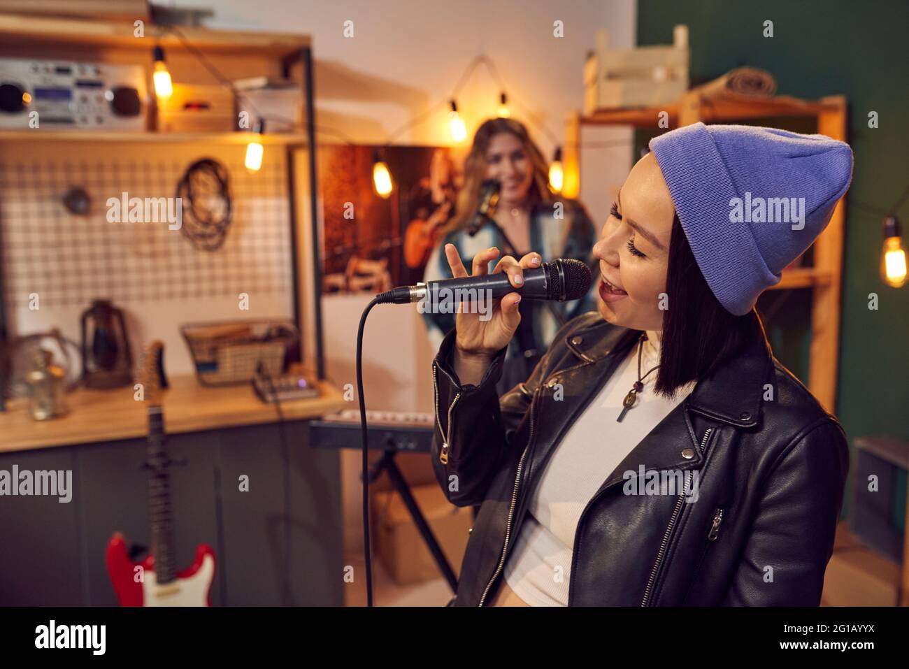 Giovane donna allegra con microfono che canta contro la sua amica che gioca la tastiera Foto Stock