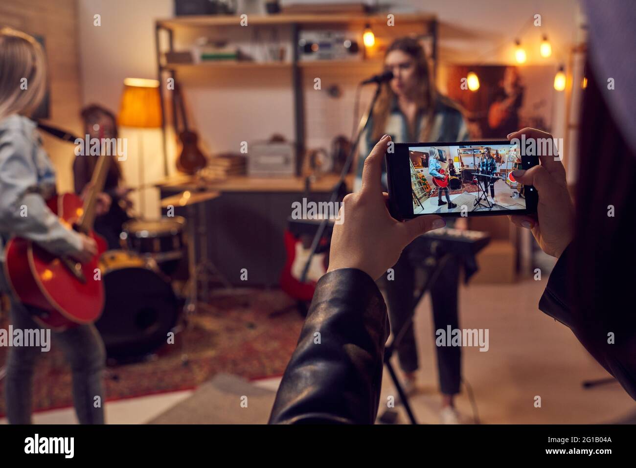 Ragazze con smartphone che prendono video della sua band che suona strumenti musicali in studio Foto Stock