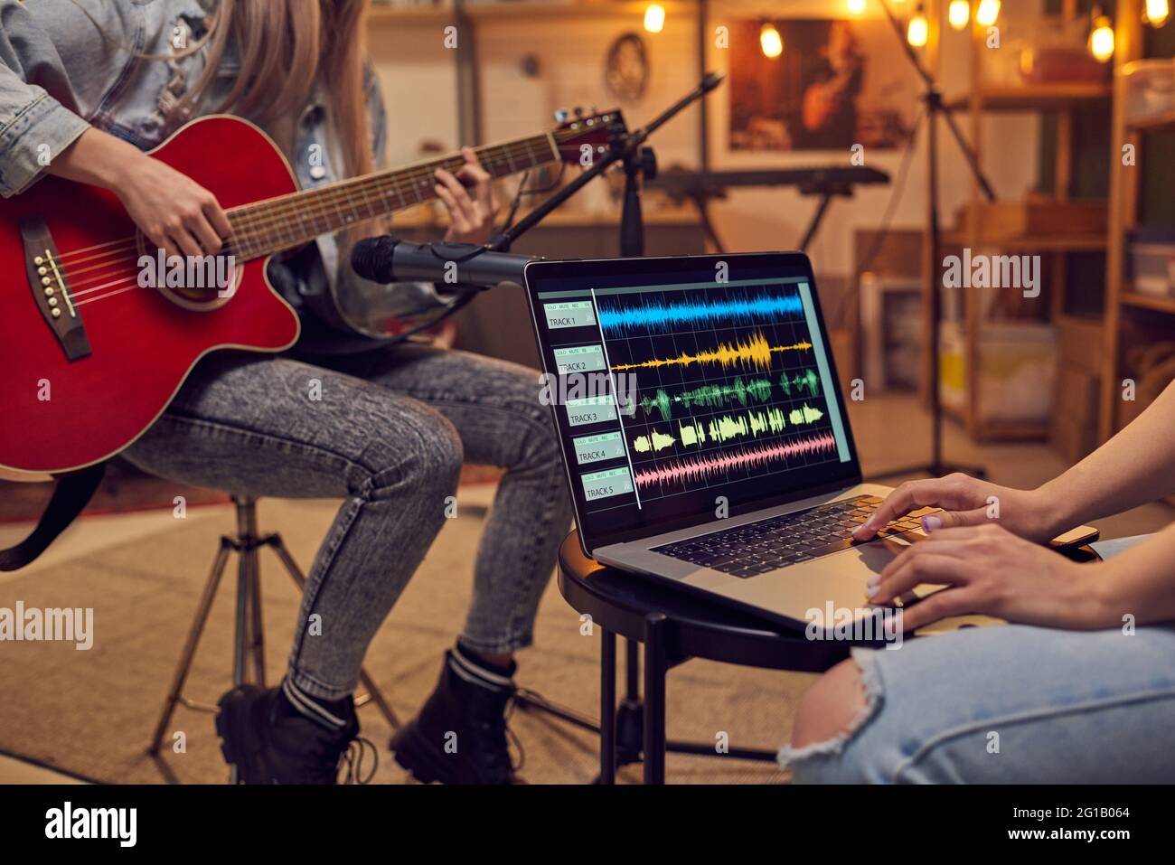 Ragazza con portatile che registra musica suonata da giovane femmina con chitarra Foto Stock