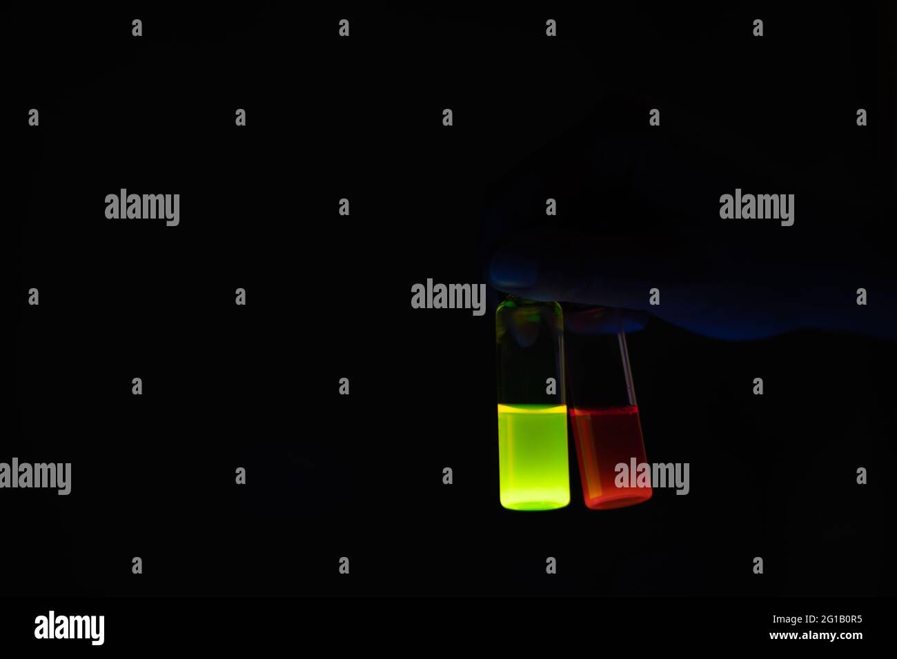 Una donna ricercatrice che tiene fiale di vetro per campioni chimici in un laboratorio organico - radioattivo - fluorescenza. Uno sfondo nero dello spazio di copia. Organico m Foto Stock