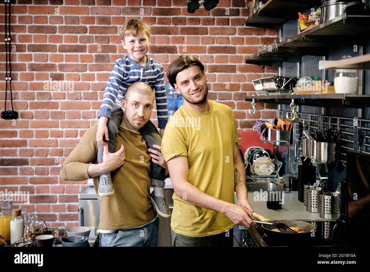 Due giovani maschi e il loro figlio carino che cucinano in cucina Foto Stock
