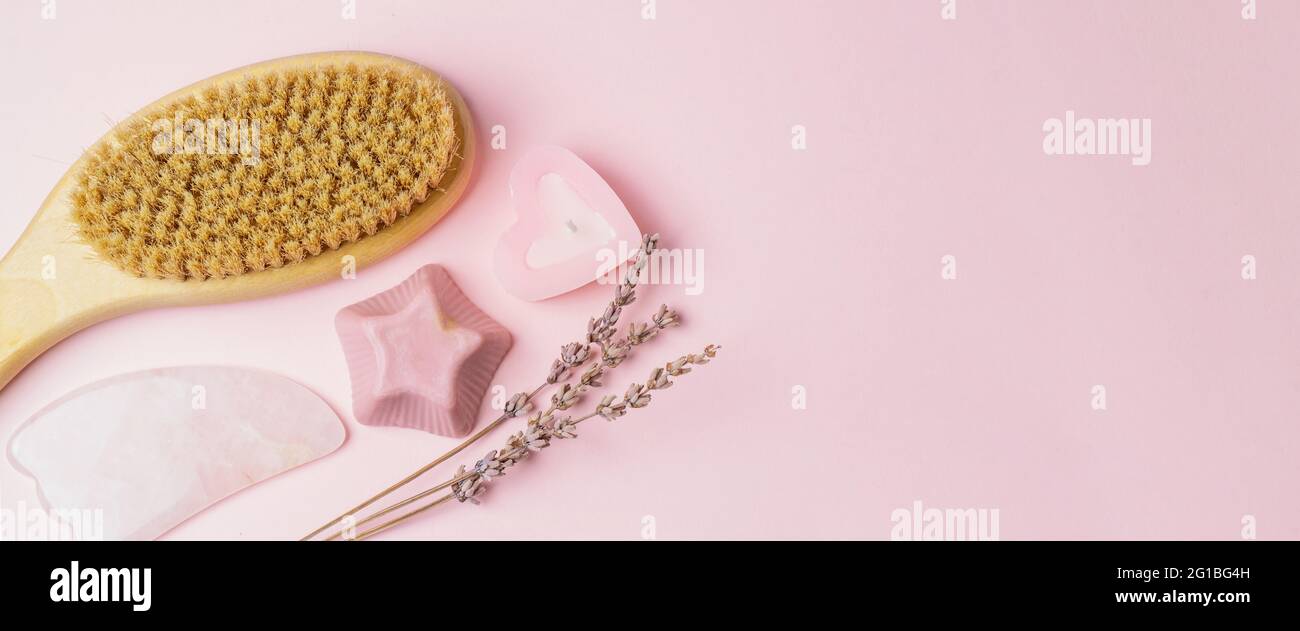 Prodotti per la cura del corpo su sfondo rosa. Sapone fatto a mano, gua sha, candela, spazzola di legno per il corpo dry massage.Skin prodotti di cura banner.Flat Lay. Foto Stock