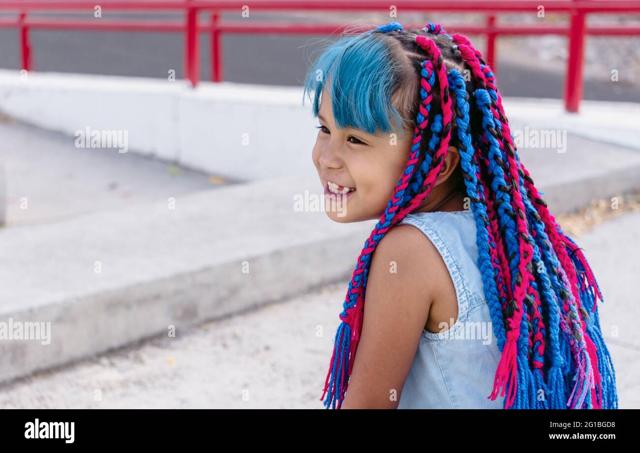 Allegro bambino etnico carino con trecce colorate seduti su scale di cemento mentre si guarda via alla luce del giorno Foto Stock