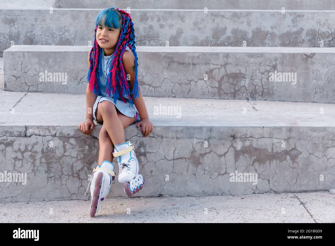 Bambino etnico sognante con trecce colorate seduti con gambe incrociate su scala mentre si guarda lontano in luce del giorno Foto Stock