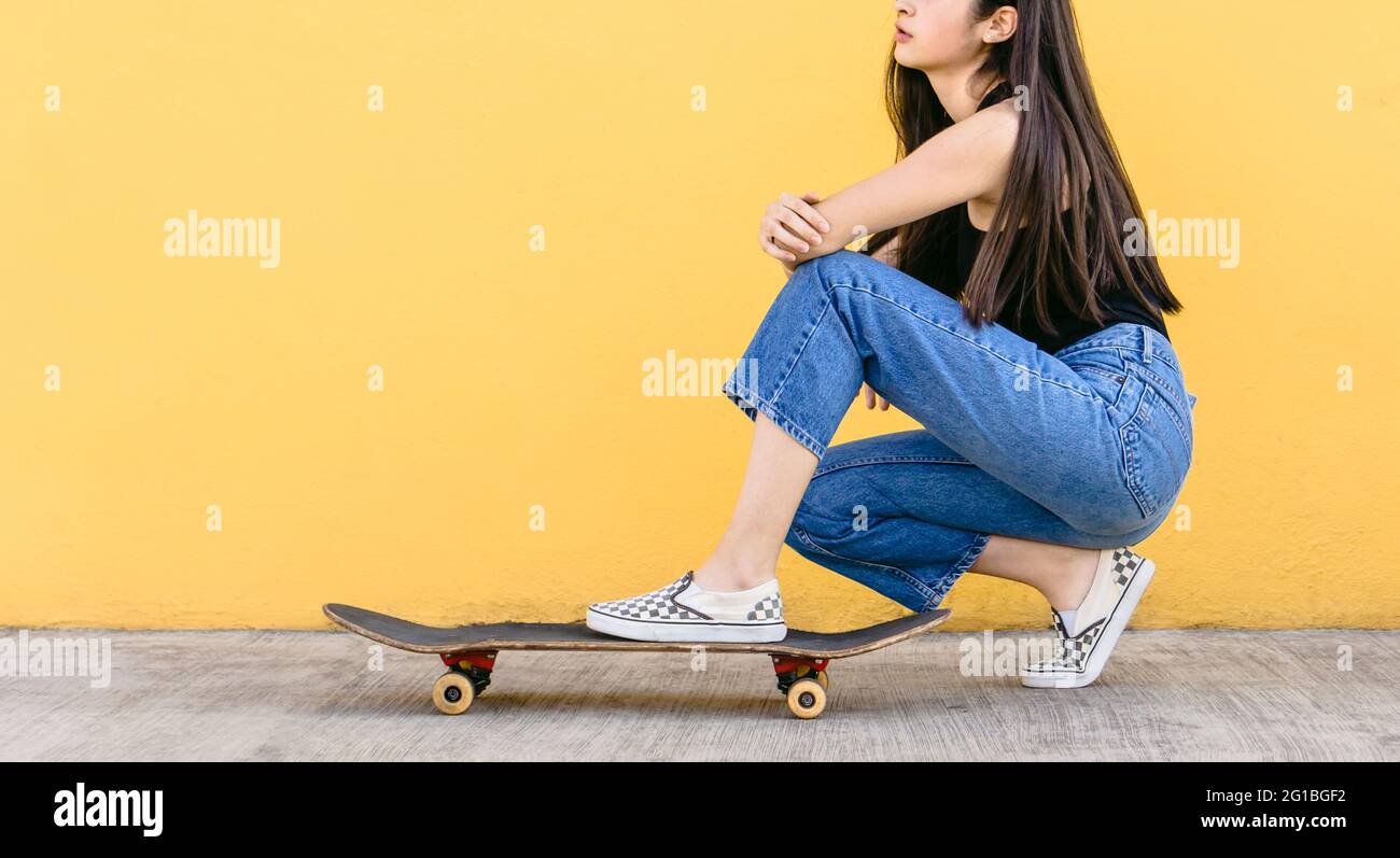 Vista laterale di una giovane e irriconoscibile skateboarder femminile sognante ritagliata in un abbigliamento casual che squadrava sul passaggio Foto Stock