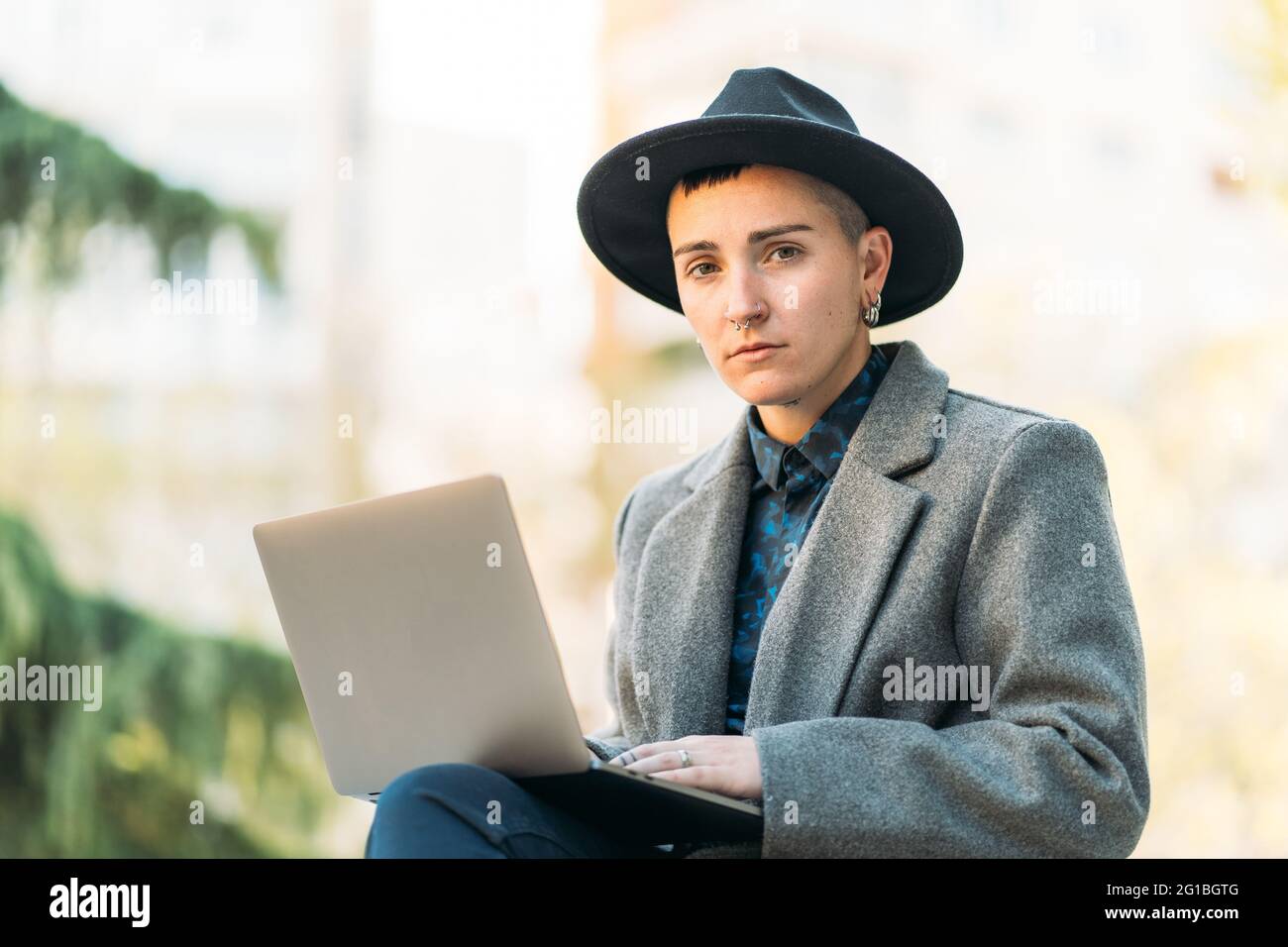 Persona androgina con mohawk in stivali e cappotto surf internet su netbook mentre si siede in città Foto Stock