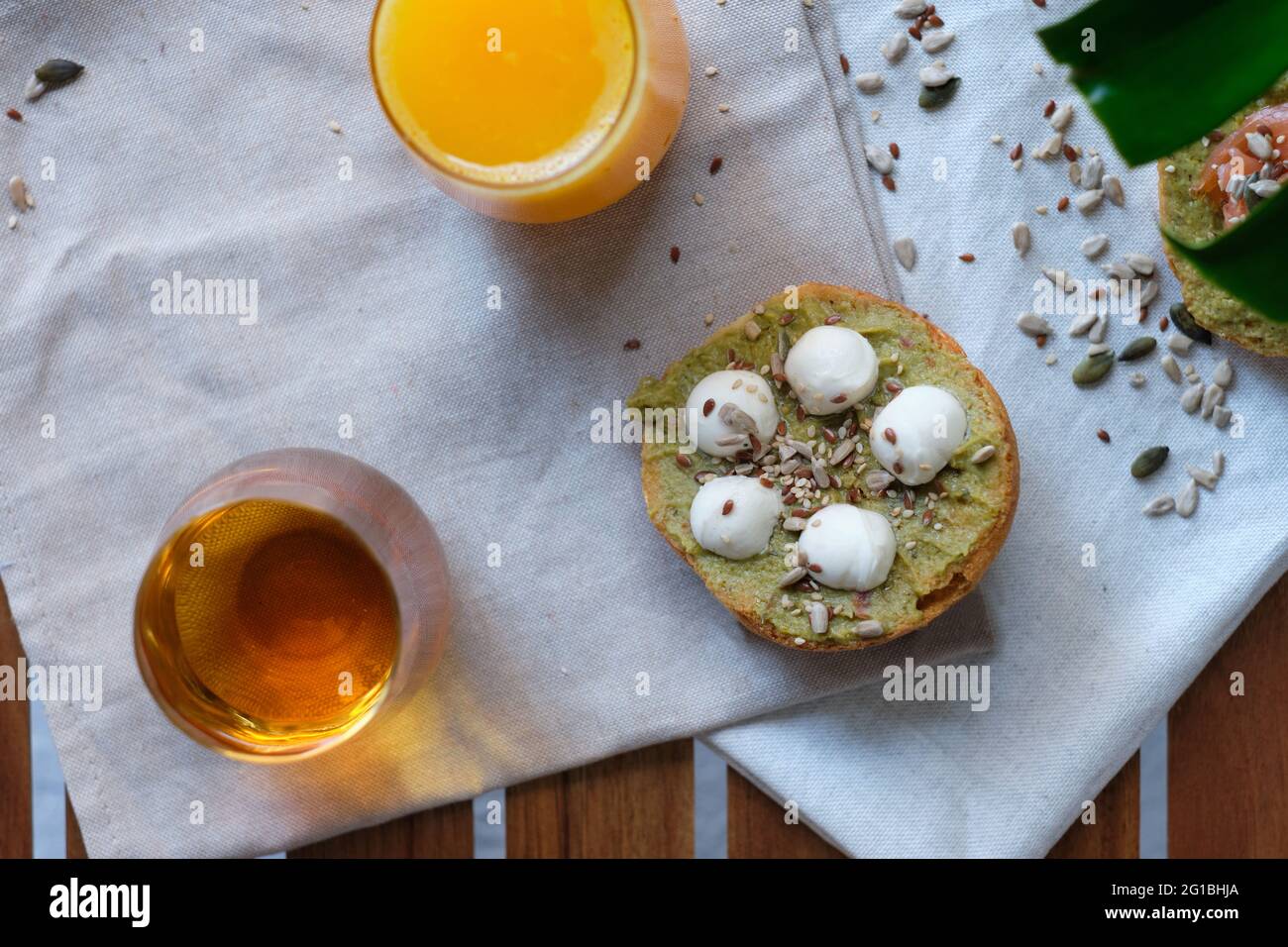 Dall'alto di toast di yummy con avocado e palline di mozzarella decorate con lino e semi di girasole e servite su tovagliolo vicino a bicchieri di arancio fresco Foto Stock