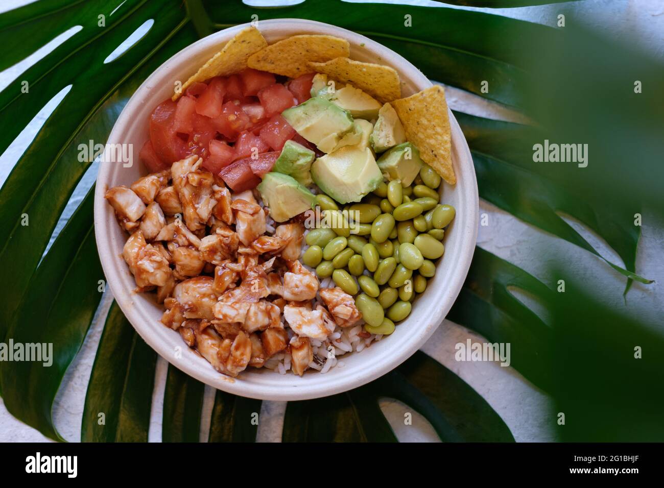 Vista dall'alto della appetitosa ciotola di riso hawaiana con pollo saucito e avocado serviti con fagioli di pomodoro freschi e nachos Foto Stock