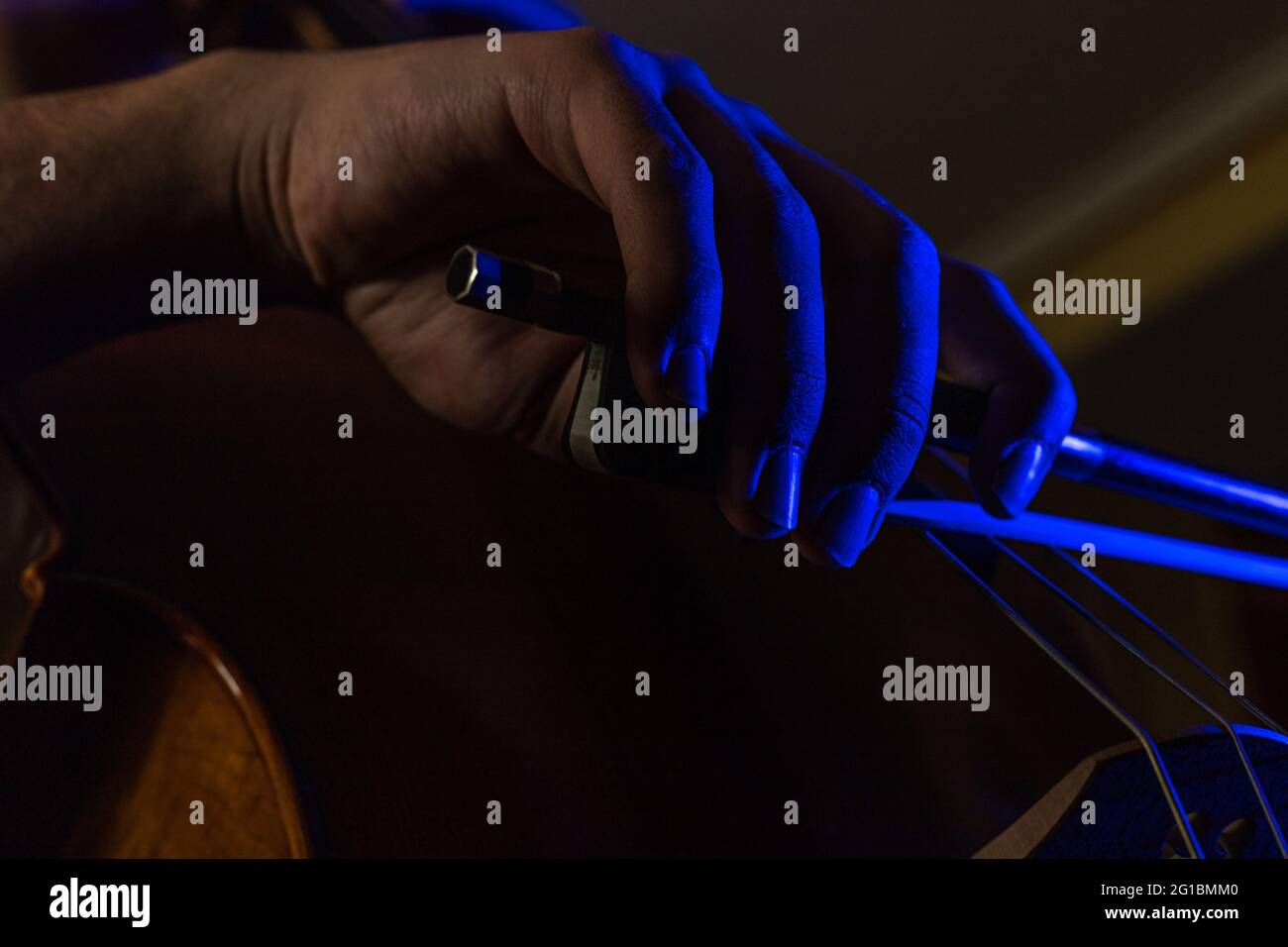 dettaglio di una mano a gomito che strofina le corde di un violoncello con luci artistiche blu e fuoco selettivo Foto Stock