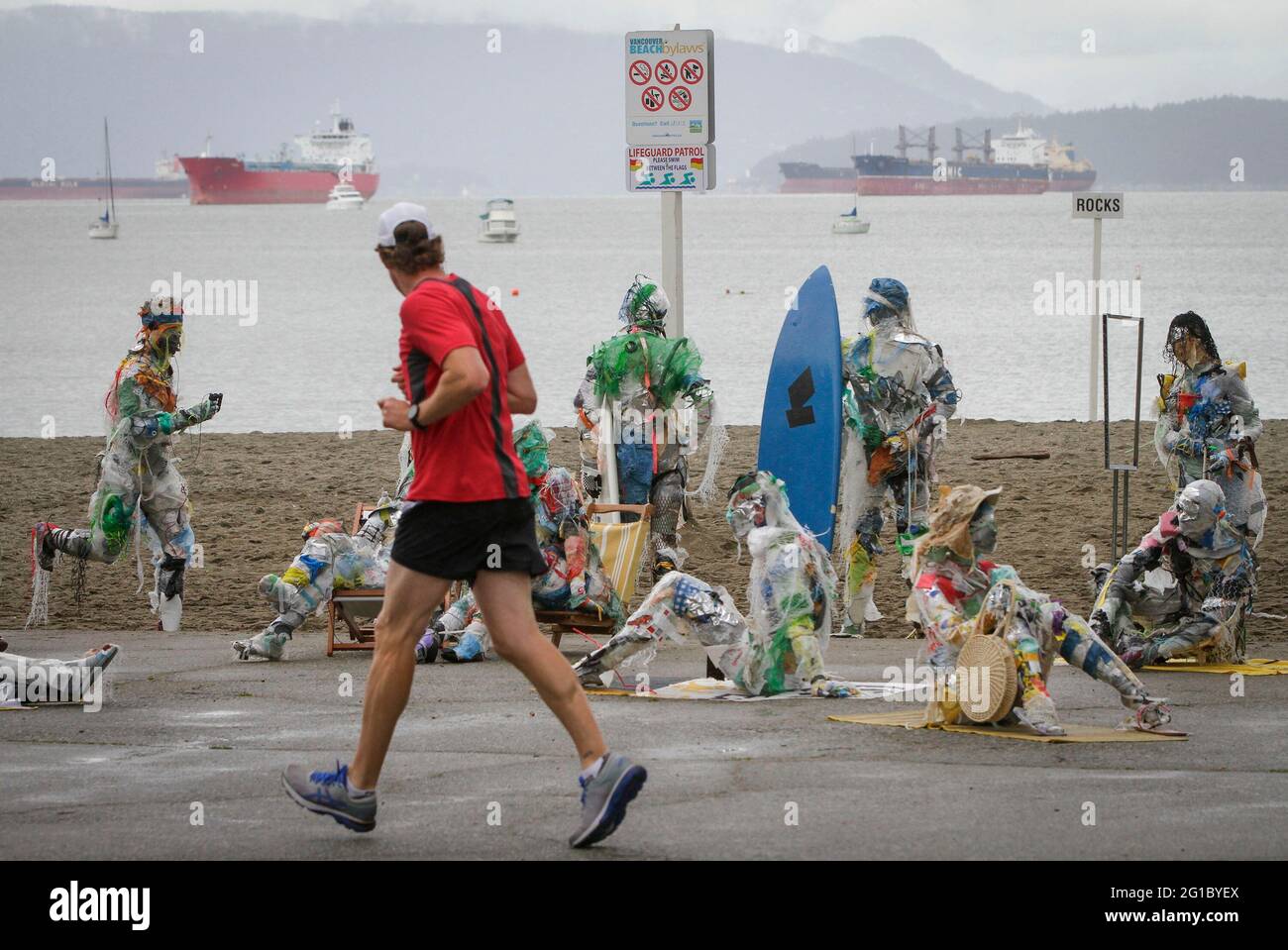 Vancouver, Canada. 6 Giugno 2021. Un uomo passa attraverso figure fatte con plastica rimossa dalle coste a Kitsilano Beach a Vancouver, British Columbia, Canada, il 6 giugno 2021. Creato dall'artista multidisciplinare Caitlin Doherty e realizzato con materie plastiche rimosse dalle coste canadesi, un insieme di figure denominate beachgoer in plastica incarnano il contributo collettivo delle persone all'inquinamento plastico, portano il tema dell'inquinamento delle coste in prima linea. Credit: Liang Sen/Xinhua/Alamy Live News Foto Stock