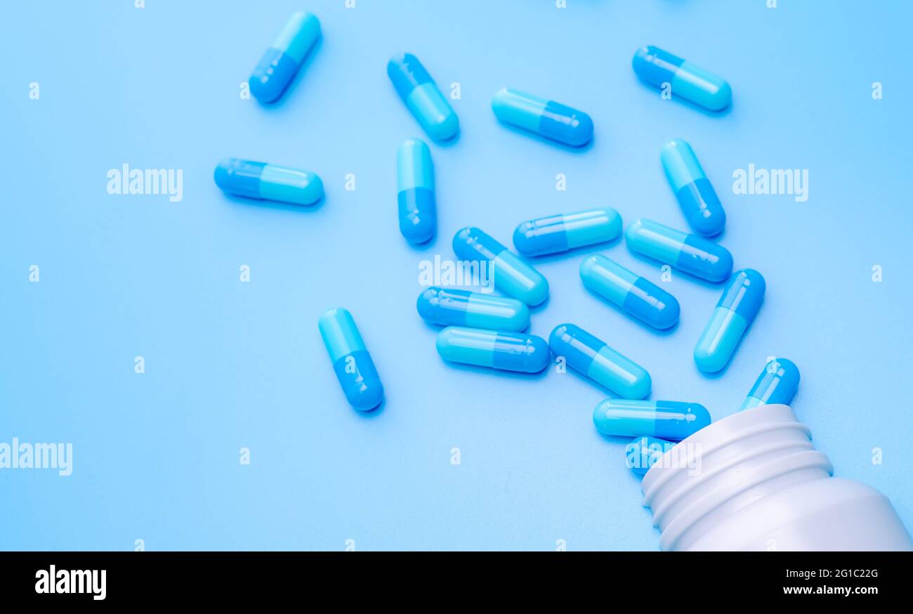 Capsule blu compresse sparse fuori del flacone su sfondo blu. Industria farmaceutica. Sviluppo di farmaci e nuove ricerche di farmaci per il trattamento emergente Foto Stock