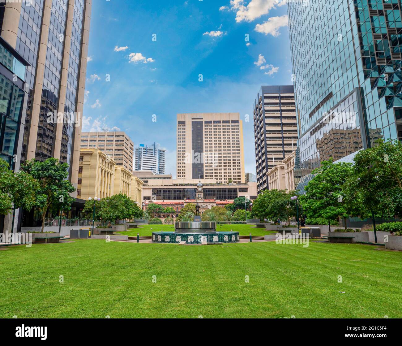 Parcheggia presso l'ufficio postale di Brisbane, Australia. Erba verde, alberi, cielo blu, hotel e uffici. Stazione ferroviaria centrale sullo sfondo. Foto Stock