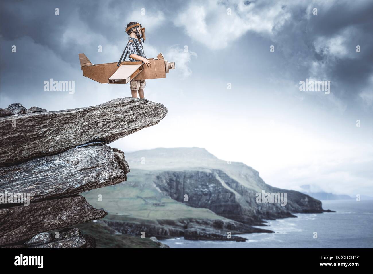 bambino vestito da aviatore con aereo di cartone su una scogliera sogna un'avventura. Foto Stock