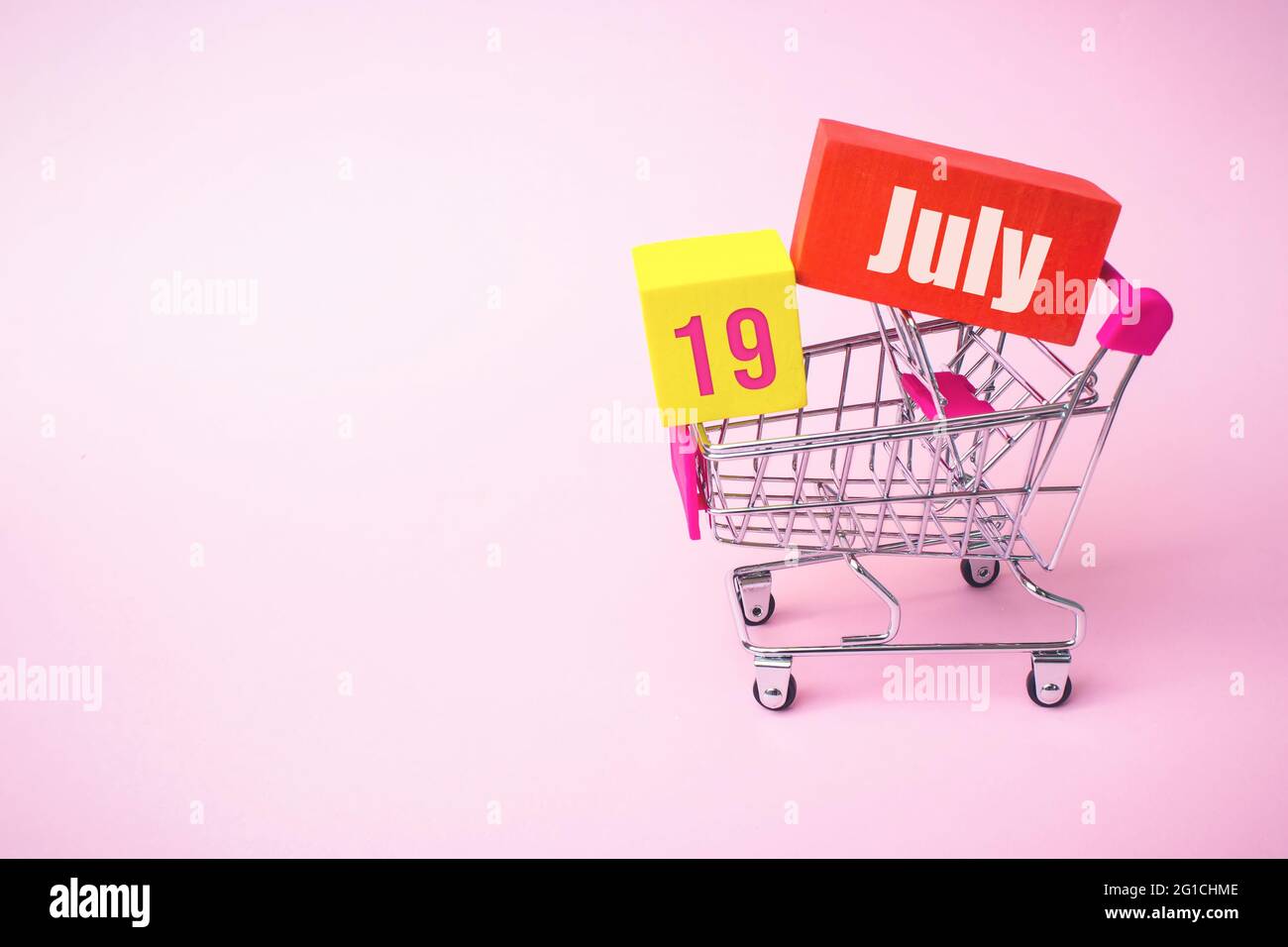 19 luglio. Giorno 19 del mese, data del calendario. Primo piano carrello giocattolo in metallo con scatola rossa e gialla all'interno con data calendario su sfondo rosa. SUMM Foto Stock