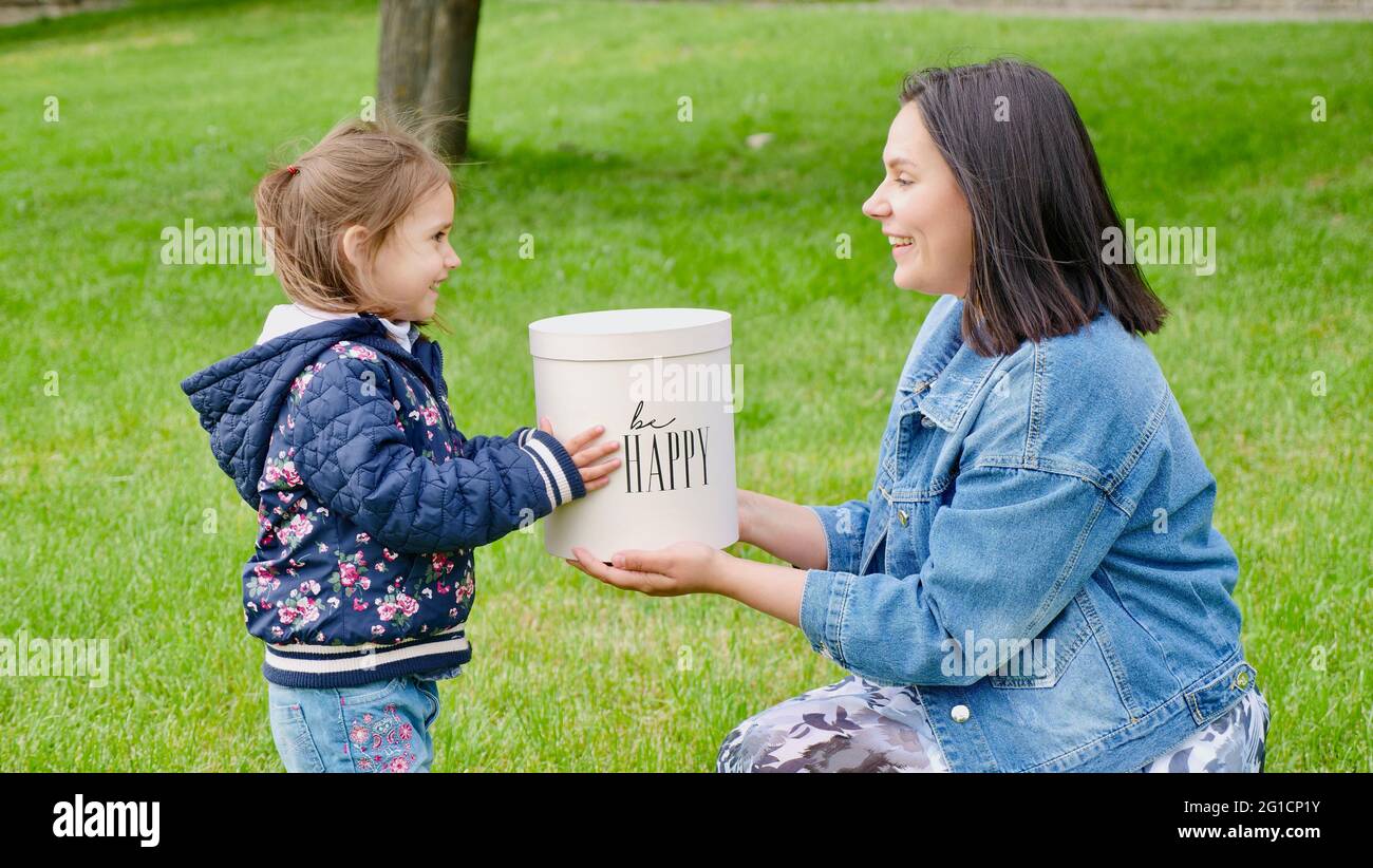 Mamma e bambina che tengono una scatola regalo con l'iscrizione essere felice da vicino senza un volto. Madre con bambino fuori Foto Stock