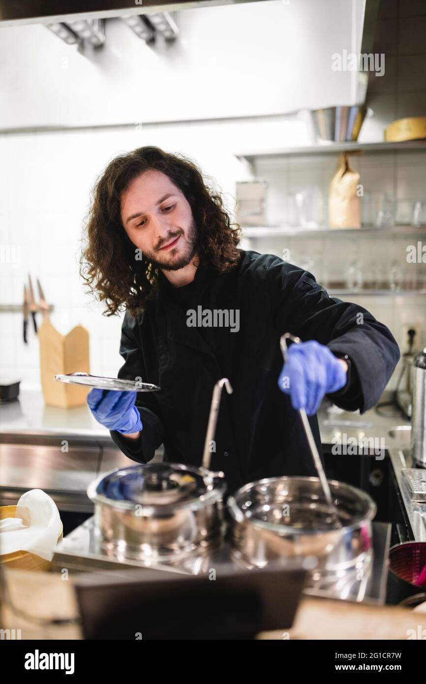 Lo chef maschile si mescola mentre prepara il cibo in cucina al ristorante Foto Stock