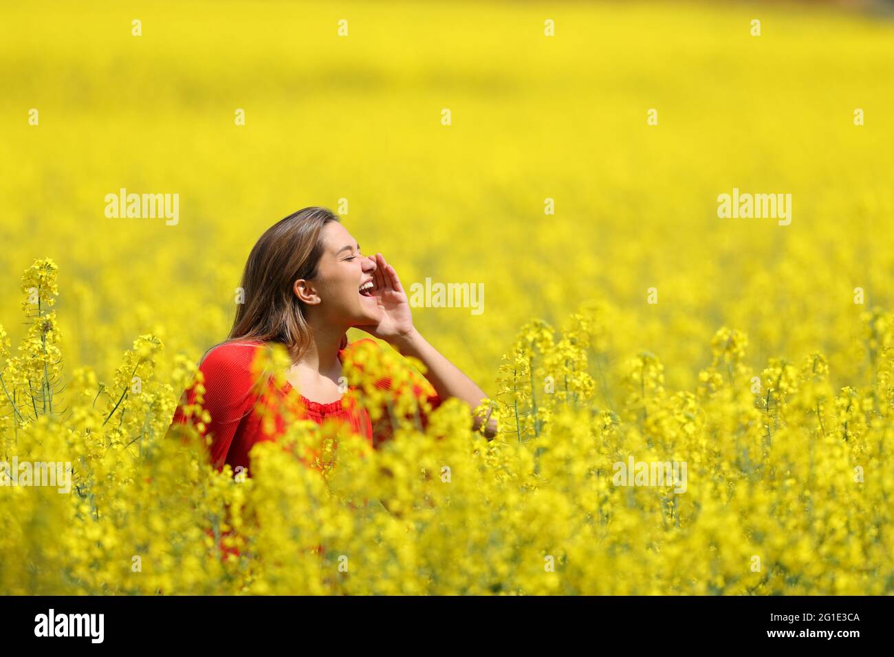 Vista laterale ritratto di una donna felice in rosso urlando in un campo giallo nella stagione primaverile Foto Stock