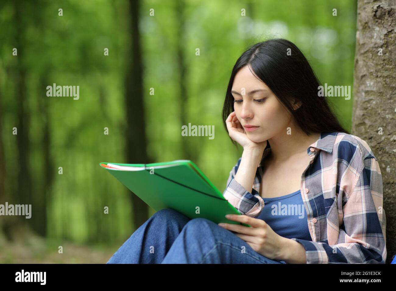 Studente asiatico che studia le note di lettura seduti appoggiandosi su un albero in un parco Foto Stock