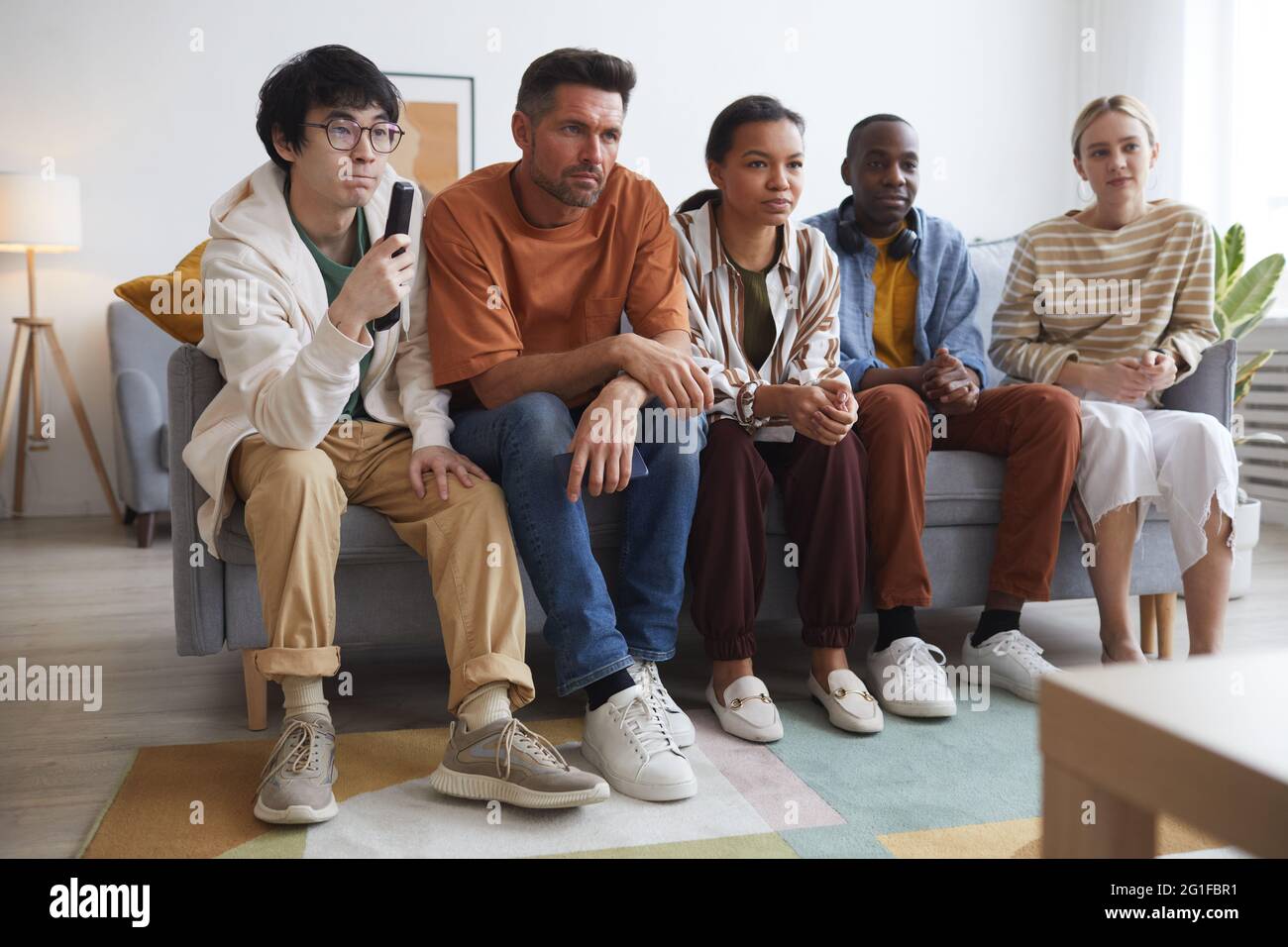 Vista completa su diversi gruppi di amici che guardano la TV a casa insieme mentre si siede in fila sul divano Foto Stock